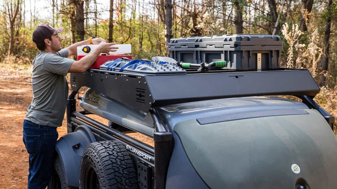 Man loading gear onto SylvanSport DuraDeck on a vehicle roof rack.
