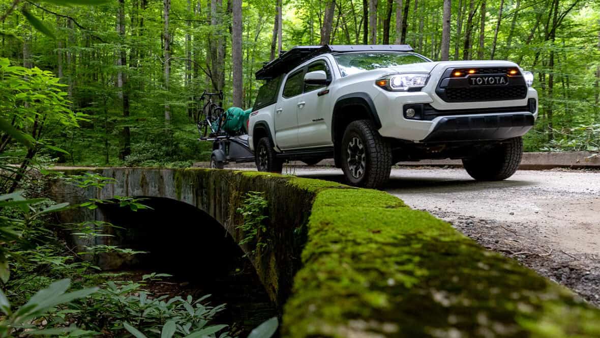 Toyota truck with kayak trailer in lush forest setting.